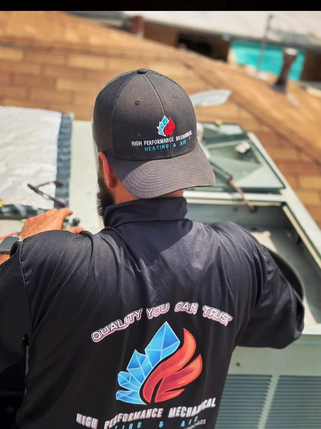 Technician in a High Performance Mechanical shirt and cap servicing an HVAC unit
